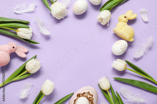 Frame made of tulips with Easter eggs, bunny figurines and feathers on lilac background