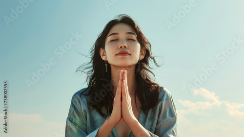 A young woman with her hands in a prayer position, praying and giving thanks to her God, against background of blue sky
