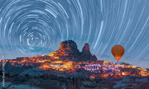 Hot air balloon flying over Goreme village with star trail at twilight blue hour - Cappadocia, Turkey 