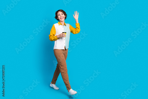 Photo of positive girl walking with latte coffee cup greeting colleagues isolated blue color background