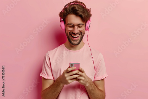 Young man on pastel studio background uses mobile phone and noise cancellation headphones head set, listens to music, has good time, enjoys his favorite tracks