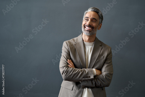 Happy middle aged business man looking away at copy space. Smiling confident 50 years old mature professional businessman executive ceo manager or entrepreneur standing at gray office wall background.