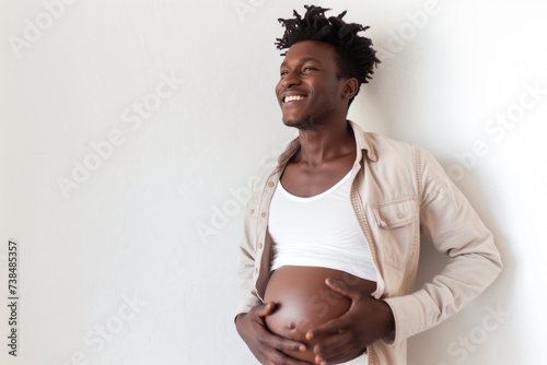 A pregnant, black, transgender African American man holding his belly against a white background with room for text. 