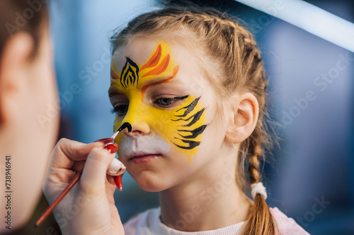 A woman professional artist paints with a brush, a colored pencil on the face of a child, a beautiful girl, face painting, makeup, watercolor drawing at a party. Photography, creative process.