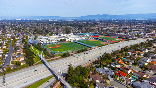 Aerial view of a high school grounds in residential neighborhood near Don Burnett bicycle pedestrian cable-stayed bridge over Interstate 280, spanning Cupertino and Sunnyvale, California