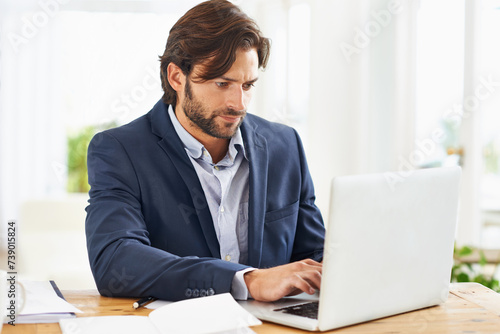 Laptop, internet and report with business man at desk in office, working on corporate review or feedback. Computer, email or website with confident young employee typing information in workplace