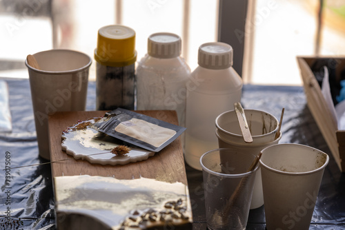 mesa de trabajo con materiales para trabajar resina epóxica, tabla de cocina, porta vaso y vasos desechables 