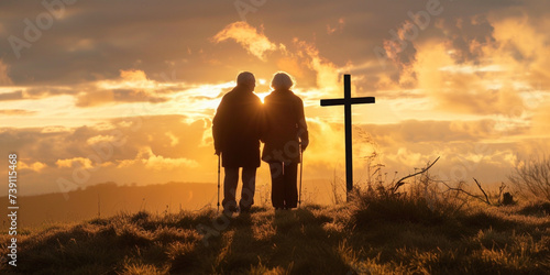 Silhouette of senior couple on high hill with cross during sunrise or sunset. Regretting sins, missing people who passed away, deeply religious person, praying, thinking about soul and meaning of life