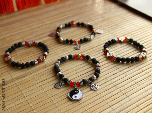 Natural lava stone bracelets with taoist yin yang symbol, lucky coins, buddhist eternal knot on chinese style bamboo wood background.