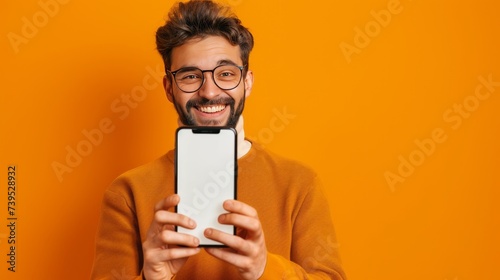 Portrait image of happy smiling casual man in eye glasses hold peep out stand behind big cell phone, smartphone, isolated on orange yellow background. Mockup empty blank white cellphone screen. 