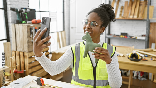 A smiling woman takes a selfie with a wooden giraffe figurine in a bright carpentry studio.