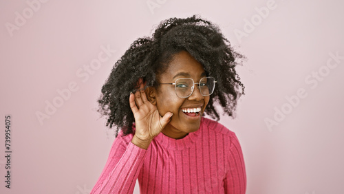 Smiling african american woman with glasses, indoors against a pink background, portraying positivity and style.