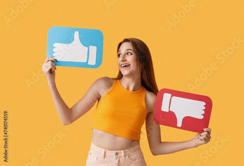 Pretty young woman holding like and dislike icons on orange background