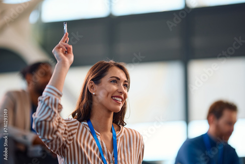 Happy businesswoman raising her hand to ask question while attending seminar in conference room