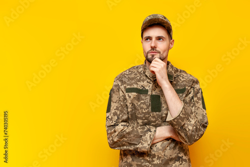 pensive Ukrainian army soldier in camouflage uniform pixel plans and thinks on yellow isolated background, Ukrainian military cadet dreams and imagines