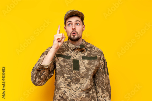 I have idea. young Ukrainian army soldier in camouflage pixel uniform pointing with finger up and surprised on yellow isolated background, Ukrainian military cadet came up with a solution