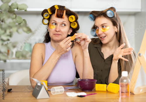 Adult woman and young woman curling hair with curlers and using eye patches