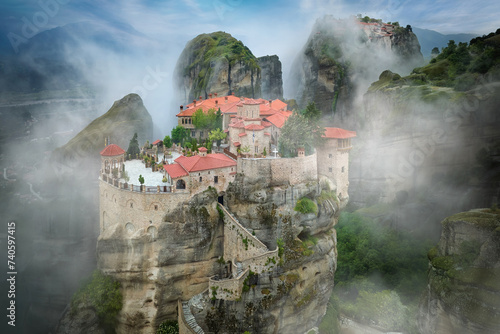 Traveling Greece: Meteora Holy Varlaam Monastery rising out of the morning mist against blue sky, nobody. Amazing mystical landscape. A UNESCO heritage site. 