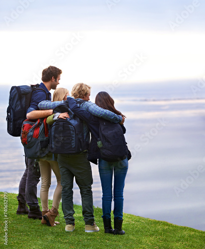 Friends, people hug with back and hiking on mountain, travel with view of horizon outdoor, ocean and backpacking in Europe. Support, trust and friendship, trekking for adventure and looking at nature