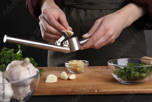 Woman squeezing garlic with press at black table, closeup