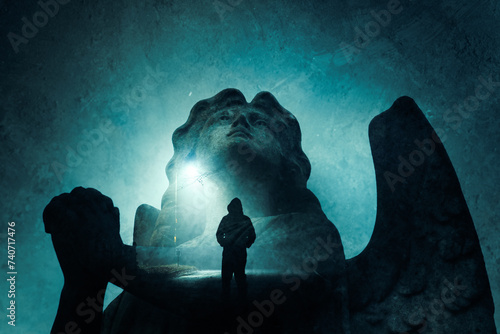A double exposure of a graveyard angel statue praying. With a spooky hooded figure. Standing on a street at night. With a grunge edit