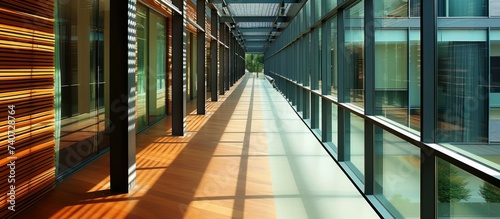 A long hallway in a building with numerous windows providing natural light, featuring wooden flooring and metal fixtures