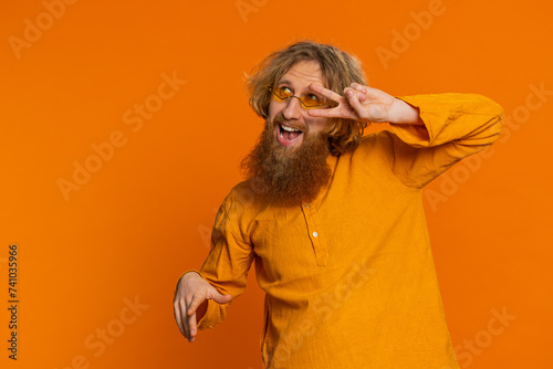 Happy smiling Caucasian man listening music and dancing disco, fooling around having fun expressive gesticulating hands relaxing on party making funny moves. Redhead guy isolated on orange background