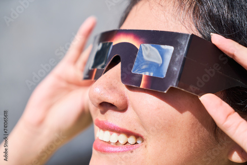 Smiling young latin woman watching an eclipse of the sun with eclipse glasses