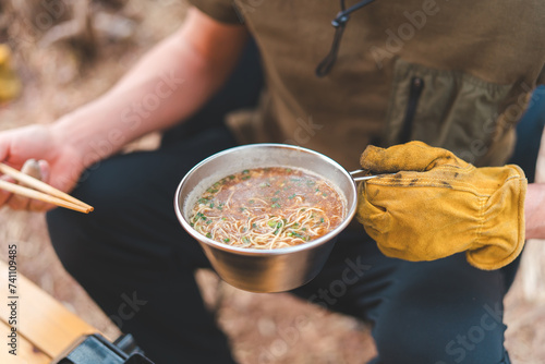 キャンプ飯でインスタントラーメン・袋麺を食べるキャンパーの男性 