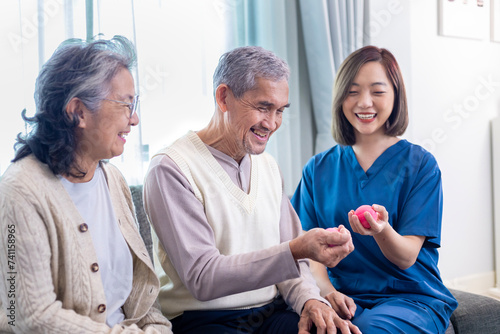 Senior couple get medical service visit from caregiver nurse while using round squishy ball for muscle strength in pension retirement center for rehabilitation and longevity post recovery process