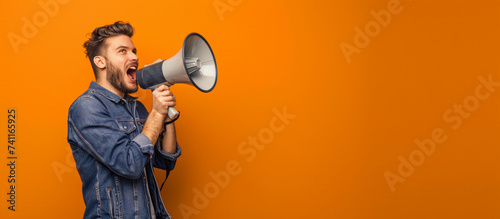 A man shouting through megaphone portrait in the studio orange background.