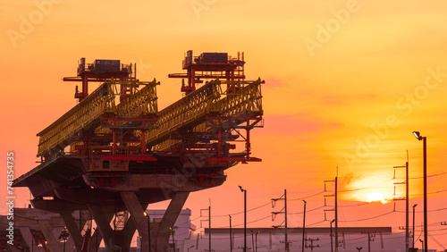 Silhouette metal launching gantry structure for installing concrete typical segment joint on foundation of elevated expressway on highway in under construction against sunset sky background 