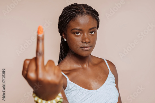 Portrait of serious angry girl, showing middle finger, looking at camera, at studio isolated over beige background. Hate, anger, angry, rude.