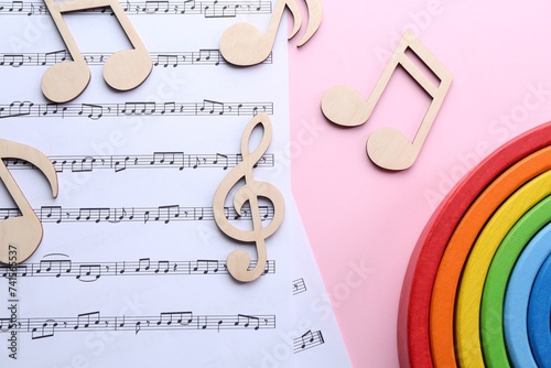 Baby songs. Music sheets, wooden notes and toy rainbow on pink background, flat lay