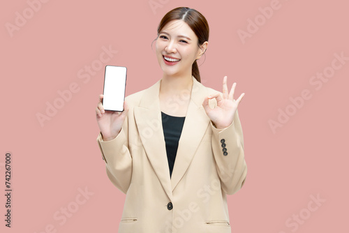 Beautiful Asian business woman showing smartphone mockup of blank screen with ok hand signal on pink background.