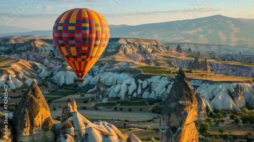A hot air balloon decorated with a colorful checkered pattern floats above. Cappadocia in Turkey