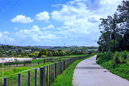 Concrete shared path curving along paddocks towards Orakei Basin. Auckand CBD skyline visible in the distance. Beautiful summer day in Auckland, New Zealand