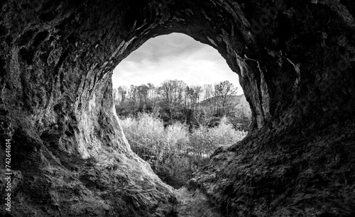 View out of the entrance of the “Grürmannshöhle“, a cave in Iserlohn-Letmathe Sauerland Germany, used as abri or shelter by early men near river Lenne. Natural underground tunnel, black and white.