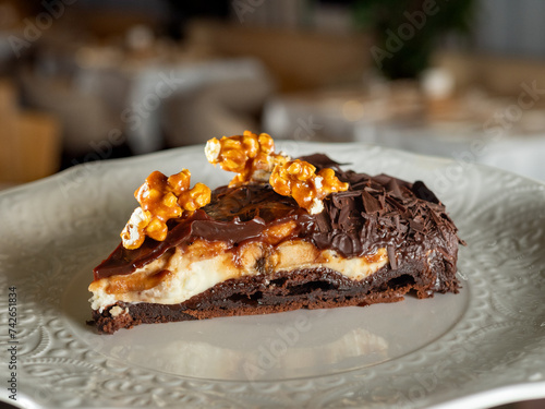 Delicious peanut and caramel cake with chocolate and walnut topped on white plate background. Piece of perfect snickers cake in minimal style. Toffee, nuts and chocolate cake in confectionery menu