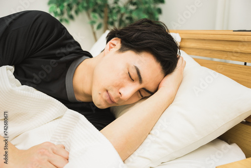 頭痛や不眠でベッドで頭を抱えて寝ている30代の男性