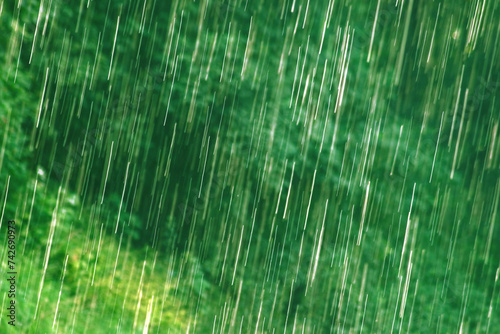 many bright raindrops of a rain shower against green background, motion blur