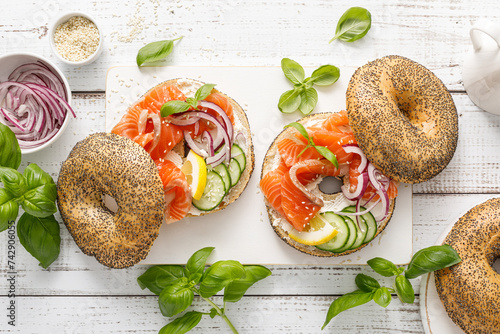 Salmon sandwiches with bagel, salted fish, fresh cucumber, onion and basil on white background, top view. Healthy breakfast with salmon toasts