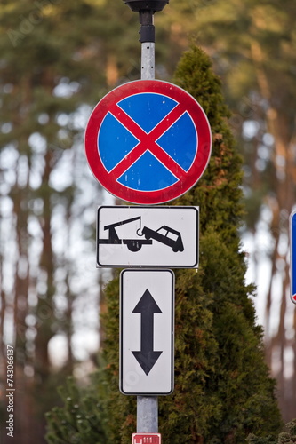 Znak zakazu parkowania i informacja o holowaniu, w tle las