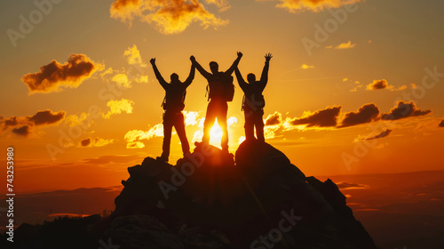 A group of hikers celebrate their achievement with raised hands against a stunning sunset atop a mountain.