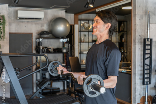 ジムでEzバー・トレーニング器具を使ってアームカール・腕トレをする若いアジア人男性 