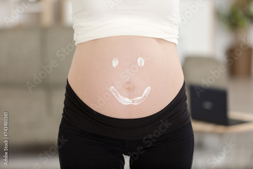 pregnant woman applying with smile shape cream to belly
