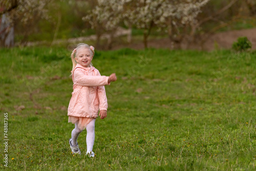 Portrait of little girl in pink outfit walking in green meadow. Child walks through clearing in spring park.