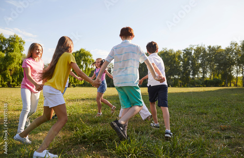 Happy, carefree children having fun during the summer break. Group of little friends dancing a round dance all together on green grass in the park on a good summer day