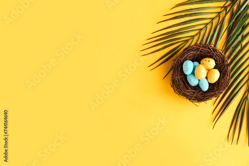 Color quail eggs in the nest on yellow background. Easter holiday concept. Copy space for the text