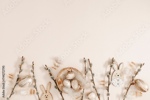 Happy Easter concept. Flat lay, top view of Easter eggs in nest, feathers, willow plant branches, rabbit on isolated pastel beige background